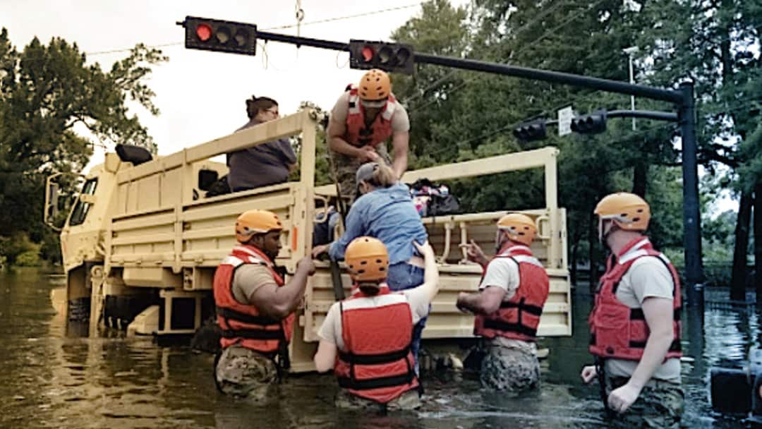 在被洪水淹没的街道上，志愿者帮助一名妇女进入卡车的床上。
