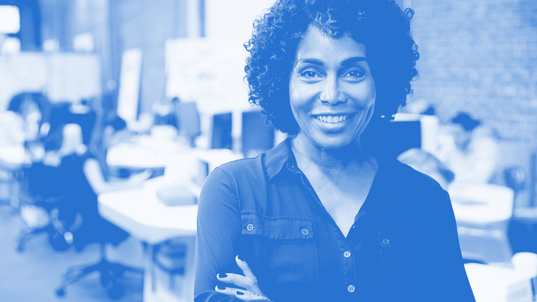 A woman stands at the forefront of the image with short, curly hair, while the background includes office desks and chairs